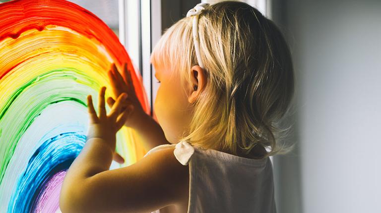 Child fingerpainting a rainbow onto a window.