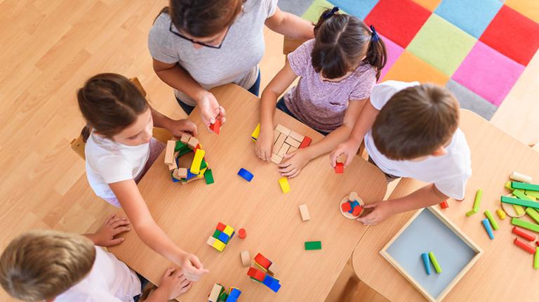  Preschool children sitting at a table playing with wooden toys.